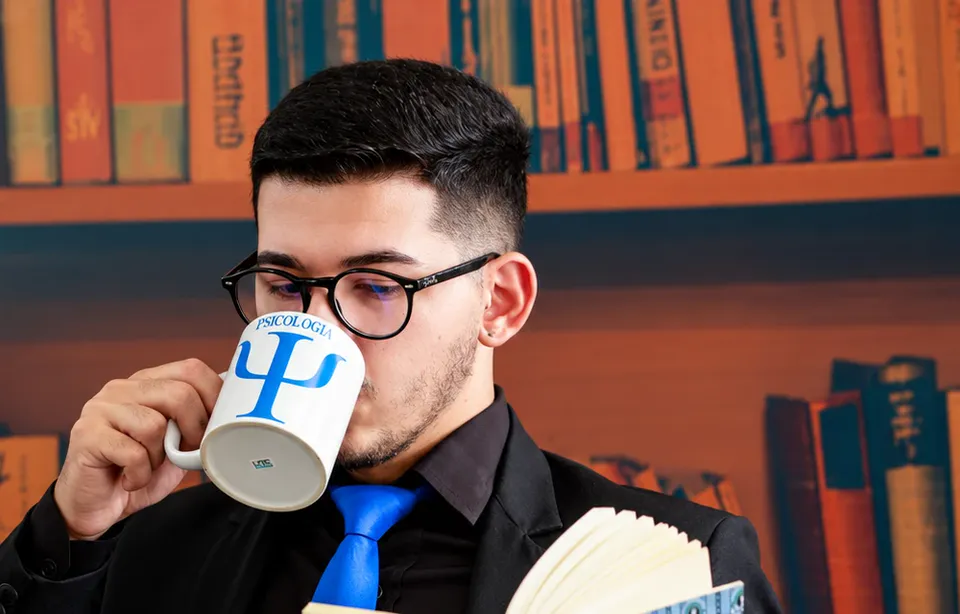Jhonatan Araújo lendo um livro e tomando café em uma mesa.